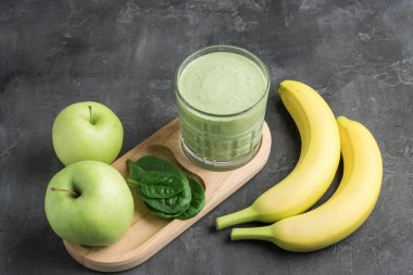 Bardakta yeşil detoks smoothie, ıspanak yapraklarından karışık vejetaryen içeceği, koyu arka planda elma ve muz meyvesi, sağlıklı beslenme kavramı..