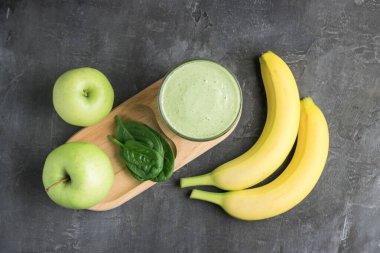 Bardakta yeşil detoks smoothie, ıspanak yapraklarından karışık vejetaryen içeceği, arka planda elma ve muz meyvesi, sağlıklı beslenme konsepti, üst görüş..