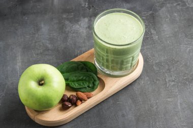 Bardakta yeşil detoks smoothie, ıspanak yaprakları, elma, muz ve fındık karışımı koyu arka planda sağlıklı beslenme konsepti..