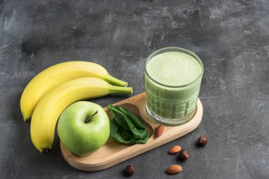 Bardakta yeşil detoks smoothie, ıspanak yaprakları, elma, muz ve fındık karışımı koyu arka planda sağlıklı beslenme konsepti..