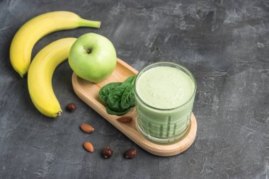 Bardakta yeşil detoks smoothie, ıspanak yaprakları, elma, muz ve fındık karışımı koyu arka planda sağlıklı beslenme konsepti..