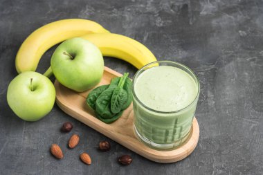Bardakta yeşil detoks smoothie, ıspanak yaprakları, elma, muz ve fındık karışımı koyu arka planda sağlıklı beslenme konsepti..