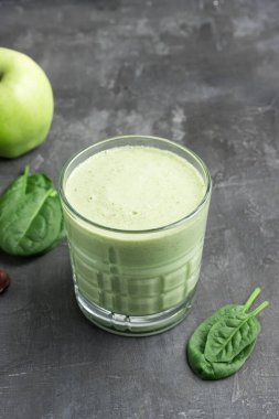 Bardakta yeşil detoks smoothie, ıspanak yapraklarından karışık vejetaryen içeceği ve arka planda elma meyvesi, sağlıklı beslenme konsepti..