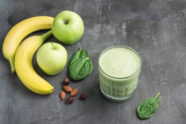 Bardakta yeşil detoks smoothie, ıspanak yaprakları, elma, muz ve fındık karışımı koyu arka planda sağlıklı beslenme konsepti..