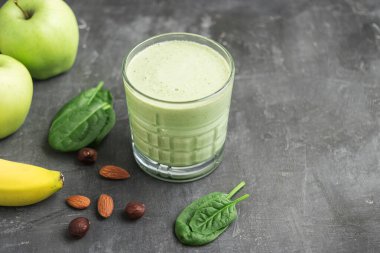 Bardakta yeşil detoks smoothie, ıspanak yaprakları, elma, muz ve fındık karışımı koyu arka planda sağlıklı beslenme konsepti..