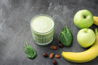 Bardakta yeşil detoks smoothie, ıspanak yaprakları, elma, muz ve fındık karışımı koyu arka planda sağlıklı beslenme konsepti..