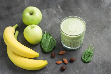 Bardakta yeşil detoks smoothie, ıspanak yaprakları, elma, muz ve fındık karışımı koyu arka planda sağlıklı beslenme konsepti..