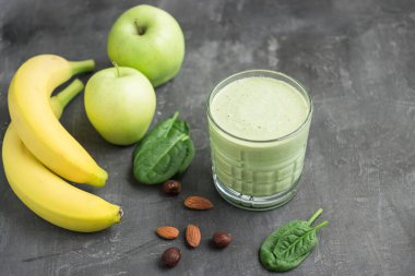 Bardakta yeşil detoks smoothie, ıspanak yaprakları, elma, muz ve fındık karışımı koyu arka planda sağlıklı beslenme konsepti..
