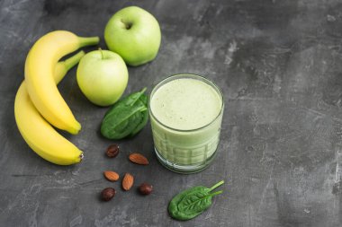 Bardakta yeşil detoks smoothie, ıspanak yaprakları, elma, muz ve fındık karışımı koyu arka planda sağlıklı beslenme konsepti..