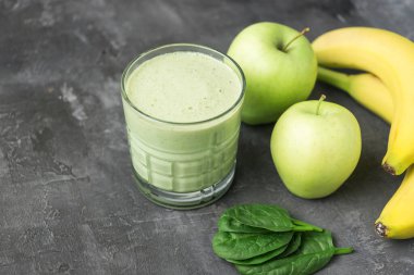 Bardakta yeşil detoks smoothie, ıspanak yapraklarından karışık vejetaryen içeceği, koyu arka planda elma ve muz meyvesi, sağlıklı beslenme kavramı..