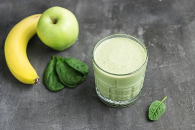 Bardakta yeşil detoks smoothie, ıspanak yapraklarından karışık vejetaryen içeceği, koyu arka planda elma ve muz meyvesi, sağlıklı beslenme kavramı..