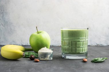 Bardakta yeşil detoks smoothie, protein tozuyla ölçme kaşığı, ıspanak yaprakları, elma ve muz meyvesi karışımı, sağlıklı beslenme konsepti..