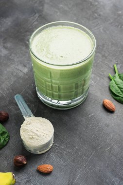 Bardakta yeşil detoks smoothie, protein tozuyla ölçme kaşığı, koyu arkaplanda karışık vejetaryen içeceği, sağlıklı beslenme konsepti..