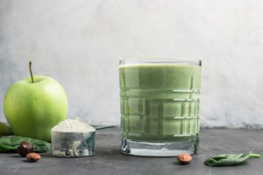 Bardaktaki yeşil detoks smoothie, protein tozuyla ölçme kaşığı, ıspanak yaprakları ve elma meyvesinden karıştırılmış vejetaryen içeceği, sağlıklı beslenme konsepti..