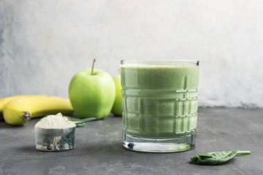Bardakta yeşil detoks smoothie, protein tozuyla ölçme kaşığı, ıspanak yaprakları, elma ve muz meyvesi karışımı, sağlıklı beslenme konsepti..