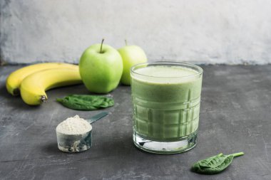 Bardakta yeşil detoks smoothie, protein tozuyla ölçme kaşığı, ıspanak yaprakları, elma ve muz meyvesi karışımı, sağlıklı beslenme konsepti..