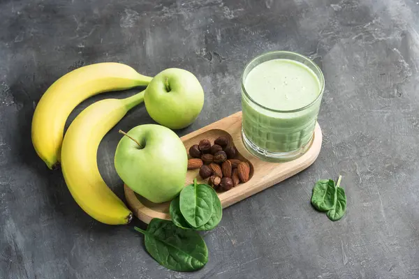 Bardakta yeşil detoks smoothie, ıspanak yaprakları, elma, muz ve fındık karışımı koyu arka planda sağlıklı beslenme konsepti..