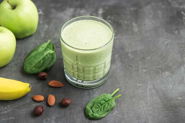 Bardakta yeşil detoks smoothie, ıspanak yaprakları, elma, muz ve fındık karışımı koyu arka planda sağlıklı beslenme konsepti..