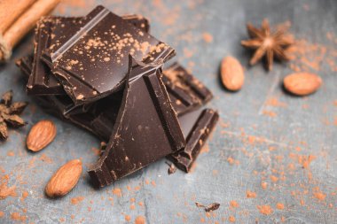 Lezzetli siyah çikolata parçacıkları ya da küpleri, doğranmış, kırılmış çikolata, badem fıstığı, tarçın çubukları ve karanlık arka planda yıldız anasonu..