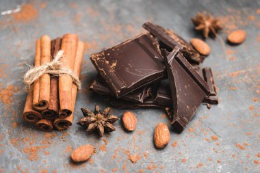 Lezzetli siyah çikolata parçacıkları ya da küpleri, doğranmış, kırılmış çikolata, badem fıstığı, tarçın çubukları ve karanlık arka planda yıldız anasonu..