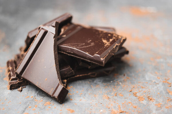 Heap of delicious dark chocolate pieces or cubes, chopped, broken chocolate bar on a dark background.