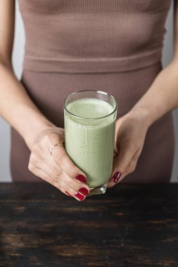 Spor kıyafetli, elinde sağlıklı yeşil vejetaryen smoothie bardağıyla tanınmayan atletik bir kadın..