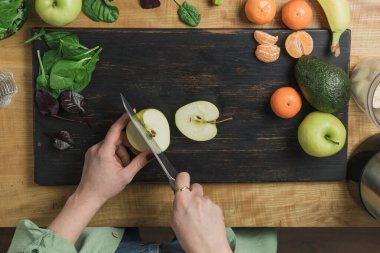 Elma kesen, ıspanak yapraklı, muzlu ve avokadolu sağlıklı vejetaryen kokteyli hazırlayan bir kadın..