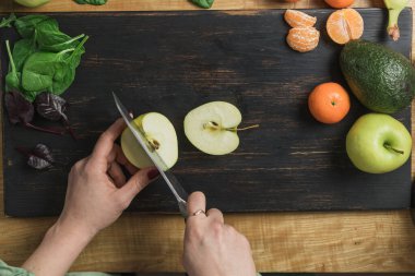 Elma kesen, ıspanak yapraklı, muzlu ve avokadolu sağlıklı vejetaryen kokteyli hazırlayan bir kadın..