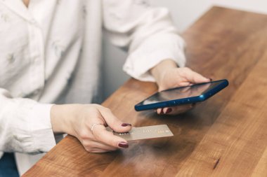Kadının elleri kredi kartını tutuyor ve online alışveriş, ödeme ya da çalışmak için bir masada cep telefonu kullanıyor.