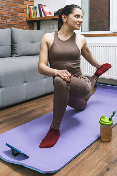 Woman training at home, doing yoga exercises and watching video on smartphone.