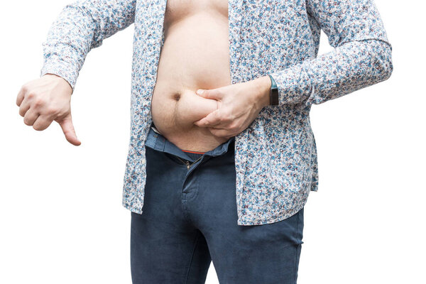 Overweight man in unbuttoned tight trousers holding his fat belly and showing big thumb down, isolated on white background.