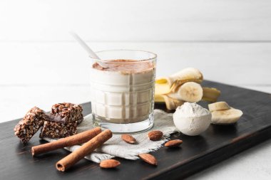 Protein içeceği, ahşap tahtada sağlıklı milkshake smoothie muz, protein tozu ölçme kaşığı, protein barı, badem fıstığı ve tarçın çubukları..