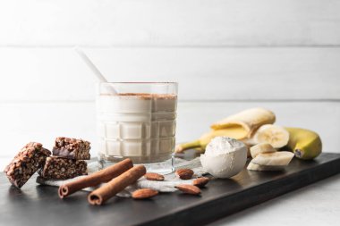 Protein içeceği, ahşap tahtada sağlıklı milkshake smoothie muz, protein tozu ölçme kaşığı, protein barı, badem fıstığı ve tarçın çubukları..