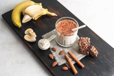 Protein içeceği, ahşap tahtada sağlıklı milkshake smoothie muz, protein tozu ölçme kaşığı, protein barı, badem fıstığı ve tarçın çubukları..