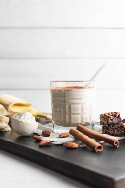 Protein içeceği, ahşap tahtada sağlıklı milkshake smoothie muz, protein tozu ölçme kaşığı, protein barı, badem fıstığı ve tarçın çubukları..