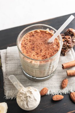 Protein içeceği, ahşap tahtada sağlıklı milkshake smoothie muz, protein tozu ölçme kaşığı, protein barı, badem fıstığı ve tarçın çubukları..