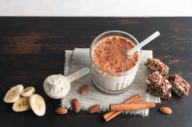 Protein içeceği, ahşap tahtada sağlıklı milkshake smoothie muz, protein tozu ölçme kaşığı, protein barı, badem fıstığı ve tarçın çubukları..