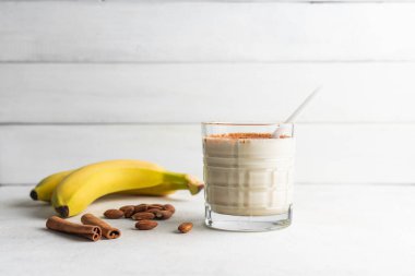 Protein içeceği, beyaz masada muzlu, badem fıstıklı ve tarçınlı sağlıklı milkshake..