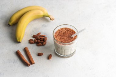 Protein içeceği, beyaz masada muzlu, badem fıstıklı ve tarçınlı sağlıklı milkshake..