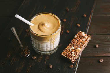 Dalgona kahvesi, çırpılmış kahve ve sütlü kokteyl. Tahta tahtada, sağlıklı bir protein çubuğuyla..