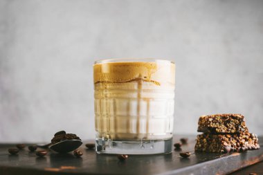 Dalgona kahvesi, çırpılmış kahve ve sütlü kokteyl. Tahta tahtada, sağlıklı bir protein çubuğuyla..