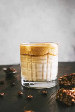 Dalgona kahvesi, çırpılmış kahve ve sütlü kokteyl. Tahta tahtada, sağlıklı bir protein çubuğuyla..