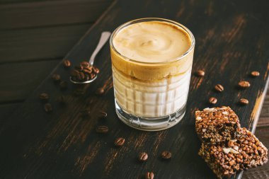 Dalgona kahvesi, çırpılmış kahve ve sütlü kokteyl. Tahta tahtada, sağlıklı bir protein çubuğuyla..