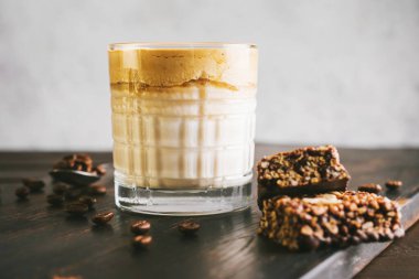 Dalgona kahvesi, çırpılmış kahve ve sütlü kokteyl. Tahta tahtada, sağlıklı bir protein çubuğuyla..