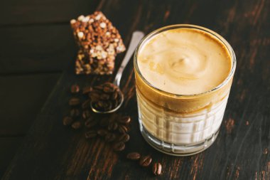 Dalgona kahvesi, çırpılmış kahve ve sütlü kokteyl. Tahta tahtada, sağlıklı bir protein çubuğuyla..