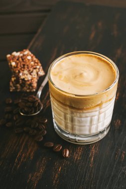 Dalgona kahvesi, çırpılmış kahve ve sütlü kokteyl. Tahta tahtada, sağlıklı bir protein çubuğuyla..