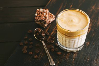 Dalgona kahvesi, çırpılmış kahve ve sütlü kokteyl. Tahta tahtada, sağlıklı bir protein çubuğuyla..