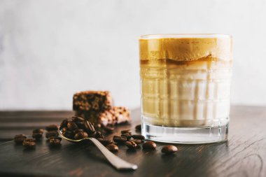 Dalgona kahvesi, çırpılmış kahve ve sütlü kokteyl. Tahta tahtada, sağlıklı bir protein çubuğuyla..