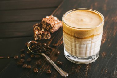 Dalgona kahvesi, çırpılmış kahve ve sütlü kokteyl. Tahta tahtada, sağlıklı bir protein çubuğuyla..