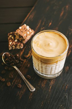 Dalgona kahvesi, çırpılmış kahve ve sütlü kokteyl. Tahta tahtada, sağlıklı bir protein çubuğuyla..